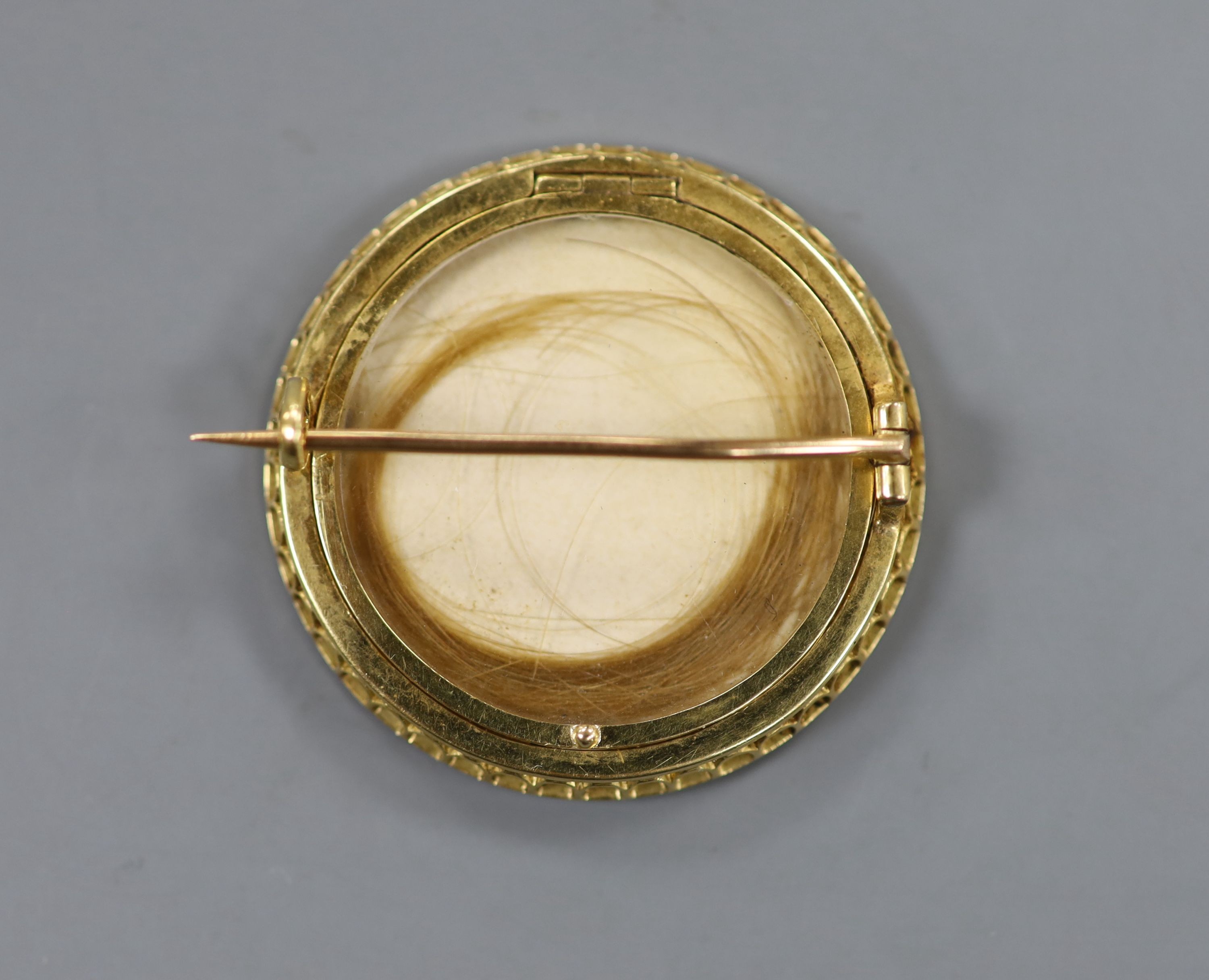 An early 20th century yellow metal and split pearl set circular brooch, inset with portrait of a young, verso with hair beneath a glazed panel, 34mm, gross weight 11.4 grams.